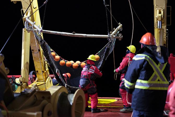 People operating large nets on the deck of a ship at night