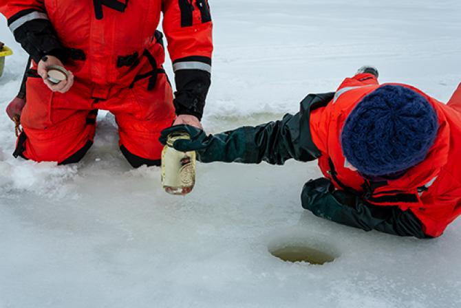 Researchers in the field gather water from a hole drilled in the ice