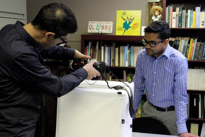 A person holds a camera over a box covered in white fabric while another person observes