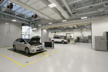 A bright, open garage space with two vehicle bays occupied by vehicles under inspection