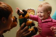 Une personne joue avec des jouets en peluche devant un nourisson qui sourit