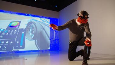 A person wearing virtual reality equipment kneels in front of a big screen