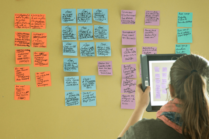 A person records post-its off a board with a tablet