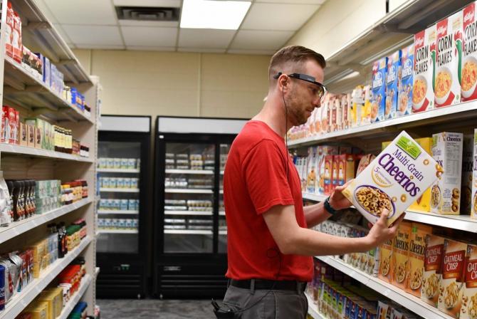 Person in a grocery aisle wears eyeglasses and examines the side of a Cheerios cereal box