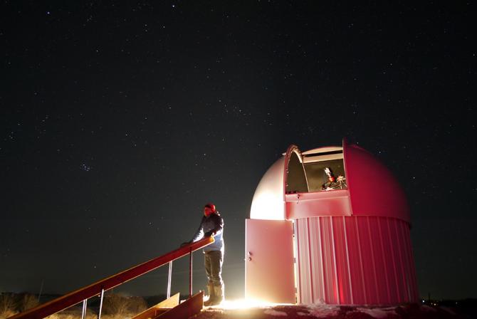 Person stands outside the open door of a dome under a starlit sky