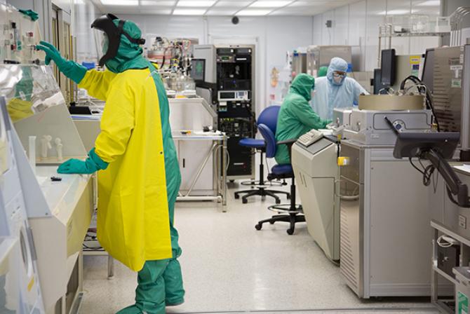 Three researchers dressed in full-body hazmat suits use research infrastructure in a lab