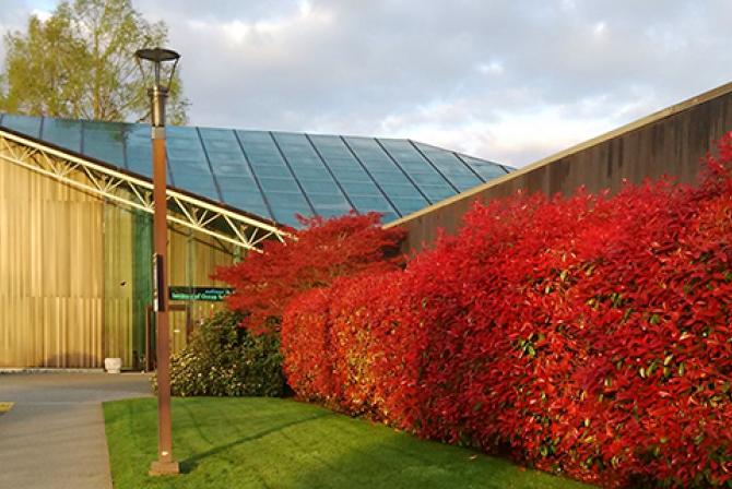 L’entrée d’une installation de recherche dont le mur extérieur est bordé d’arbustes rouges
