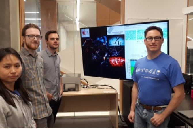 Four people stand by a large screen