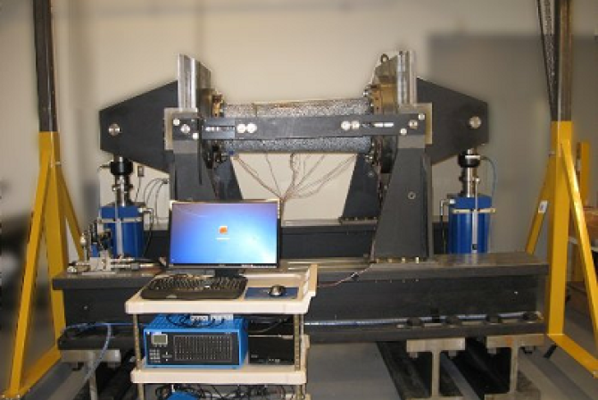 Frontal view of a tube bending machine, with a computer and controls set on a trolley next to it.
