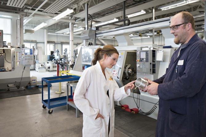 Two people manipulate a machined part in a research facility.