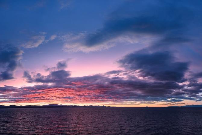 Purple-tinted sky and clouds over a vast area of water.