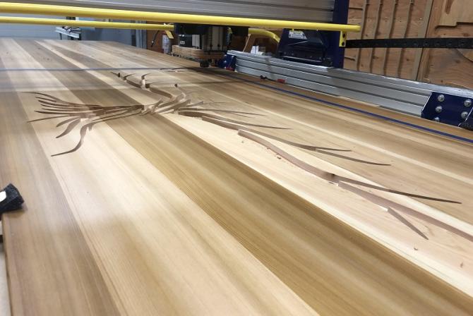 Une machine découpe des formes dans une grande planche de bois.