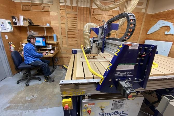 From a workstation, a person operates the ShopBot to cut wood.