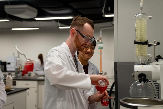 Un chercheur verse un liquide rouge d'une fiole dans une autre plus petite.