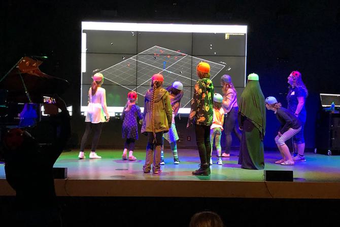 Un groupe de personnes portant des casques avec des capteurs font face à un grand écran sur une scène.