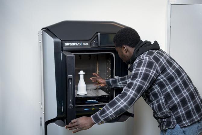 A person removes an item from a 3D printer.