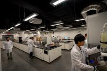 Des personnes portant des sarraus de laboratoire sont occupées à différents postes dans un grand laboratoire.