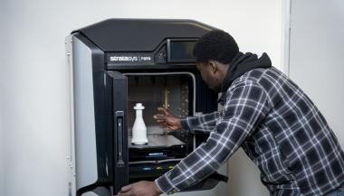 A person removes an item from a 3D printer.